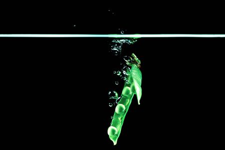 Fresh pea dropped into a water on dark background isolate.の写真素材