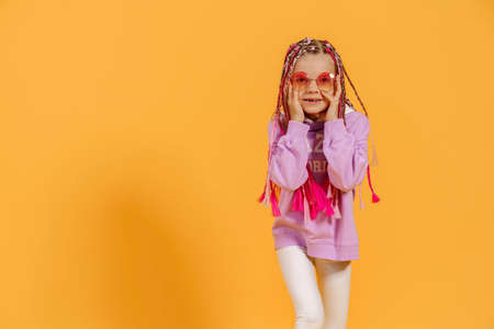 Stylish girl in rounded glasses with pink dreadlocks posing on a yellow background. Beauty, fashion.の写真素材