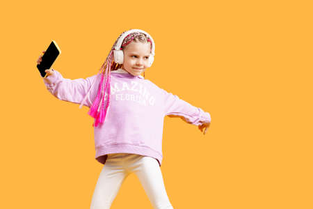 Adorable child in rounded glasses with pink dreadlocks listen to music playing in earphones and...