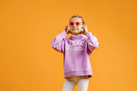 Adorable child in rounded glasses with pink dreadlocks listen to music playing in earphones on...
