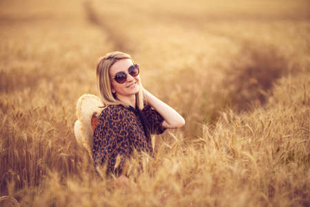 woman in animal print dress, straw hat in front of Sun in middle of wheat field with pleasure , enjoying summer holidays.の写真素材