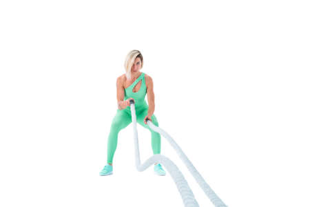 Woman doing exercises with battle rope. Photo of muscular model in military sportswear isolated on white background. Strength and motivationの写真素材