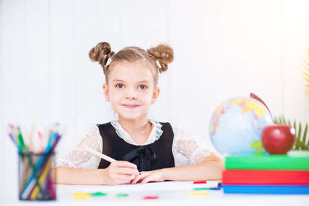 Happy smiling pupil at the desk. Girl in the class room with pencils, books. Kid girl from primary...
