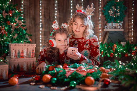 Mother and daughter looking the phone next to the christmas tree and shopping online.