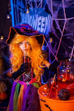 Little beautiful girl in a witch costume celebrates Happy Halloween party in interior with pumpkins.の写真素材