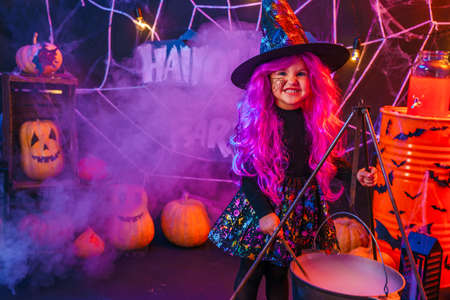 Little beautiful girl in a witch costume celebrates Happy Halloween party in interior with pumpkins.の写真素材