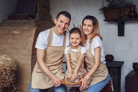 Concept of ceramic art and hobby. Happy family of three people making potter and using wheel circle. They sitting in cozy room or work place studio and working with raw and wet clay.の写真素材