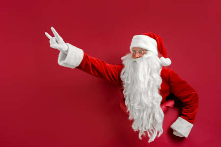 Santa man breaks through hole in paper like super man. Space for text. Holiday poster design, banner.の写真素材