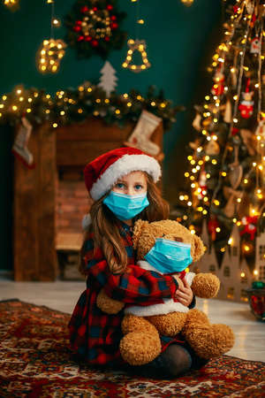 Portrait of cutel little child girl in medical mask playing with Taddy bear, New year holiday concept. Covid-19 concept.の写真素材