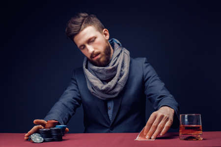 Stylish bearded Man in suit and scarf playing in dark casino, smoking cigar, drink whiskey.の写真素材