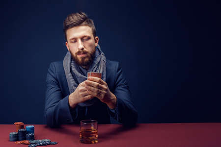 Stylish bearded Man in suit and scarf playing in dark casino, smoking cigar, drink whiskey.の写真素材