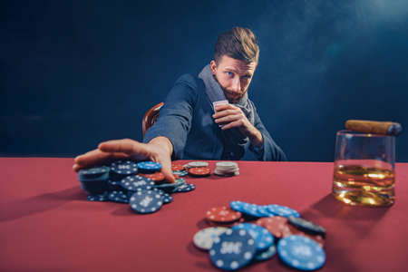 Stylish bearded Man in suit and scarf playing in dark casino, smoking cigar, drink whiskey.の写真素材