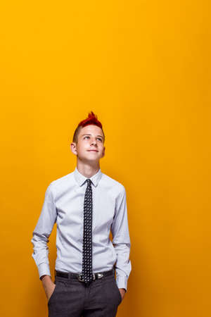 Portrait of thoughtful teen boy looks up and poses indoors. Yellow isolated background.