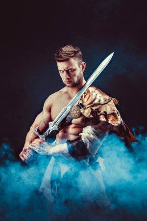 Portrait of angry gladiator with sword looking up against of black background. Isolatedの写真素材