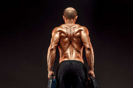 Muscled shirtless male model showing his back muscles on dark background isolate.