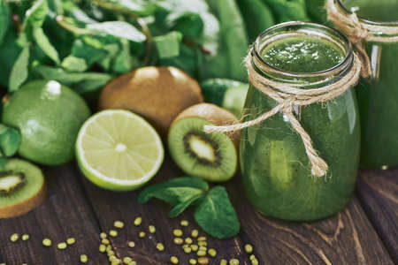 Blended green smoothie with ingredients on the stone board, wooden table selective focusの写真素材