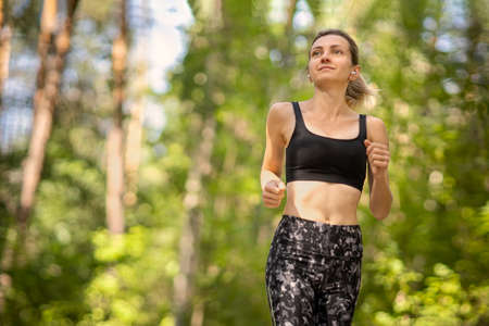 Beautiful young woman runner in a green forest.の写真素材