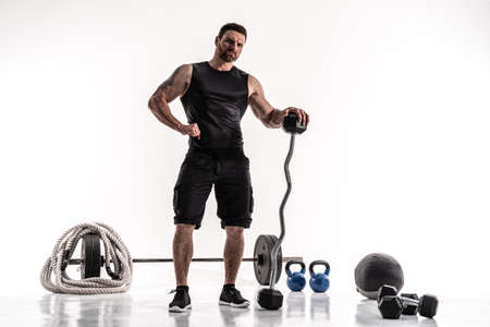 Aggressive bearded strong muscular Man in sportswear with barbell and sport equipment on white...