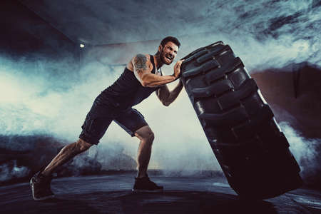 Bodybuilding training, bearded strong sportsman with muscular body lifting heavy wheel in gym.の写真素材
