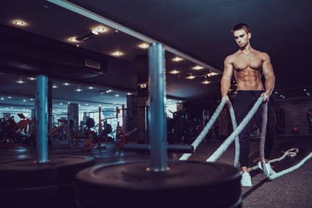 Fitness man working out with battle ropes at gym.の写真素材