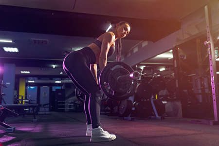Attractive fit sexy woman in the gym crouches with a barbell. Woman training back.の写真素材
