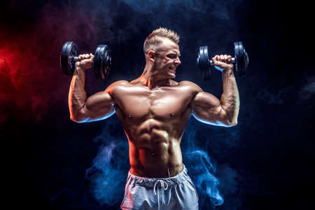 Handsome bodybuilder doing Exercise for the shoulder muscles, deltoid with dumbbell. Studio shot. Smoke.の写真素材
