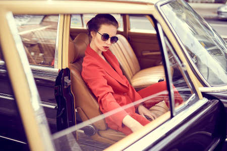 Beautiful young woman wearing red costume and sunglasses sitting in retro carの写真素材