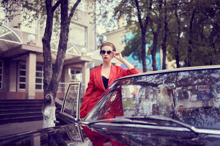 Beautiful young woman wearing red costume while standing near retro car