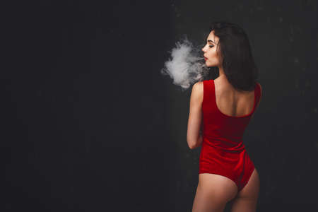 Young sexy woman in red body is vaping.の写真素材