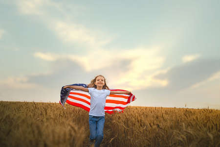 Adorable patriotic girl wearing an American flag in a beautiful wheat fieldの写真素材