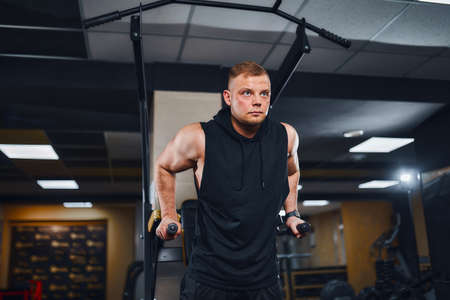 Strong muscular man doing push-ups on uneven bars in gym. Workout lifestyle concept.