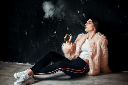 Woman in pink fur coat smoke electronic cigarette.