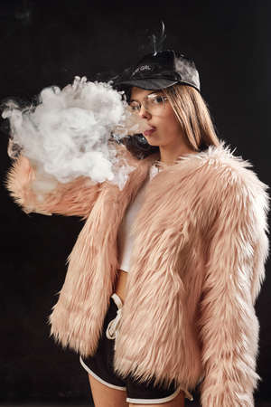 Woman in pink fur coat smoke electronic cigarette.