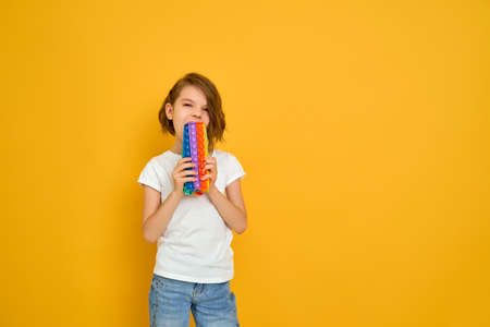 little girl holding pop it antistress toy on yellow background