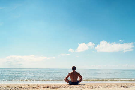 Man meditates on the sandy beach view from the backの写真素材