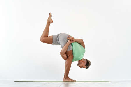 back view of sporty man practicing yoga in yoga class, making stretching back. Healthy lifestyle,...