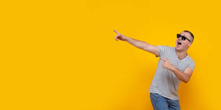 Portrait of funny young man in casual clothes pointing index fingers aside up isolated on yellow orange wall background in studio. People sincere emotions lifestyle concept. Mock up copy spaceの写真素材