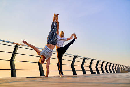 Couple doing practicing yoga together on nature outdoors . Morning exercises at the sunrise.