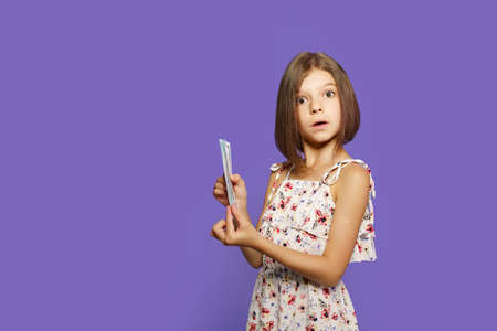 Teen girl in summer dress standing isolated with US dollar money banknotes over velvet or purple studio background.の写真素材
