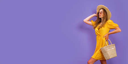 Beautiful young woman in white dress, summer straw hat, sunglasses, straw bag isolated on pastel violet background.の写真素材