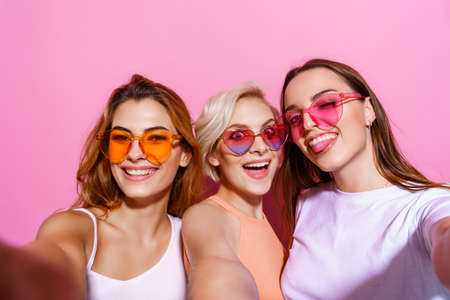 Self portrait of three funny, funky, emotional, expressive, pretty girls, gesture posing on pink background, celebrating birthday, womens day, springの写真素材