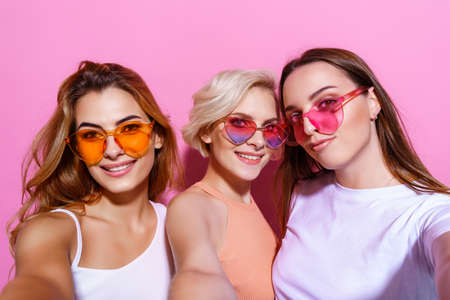 Self portrait of three funny, funky, emotional, expressive, pretty girls, gesture posing on pink background, celebrating birthday, womens day, springの写真素材