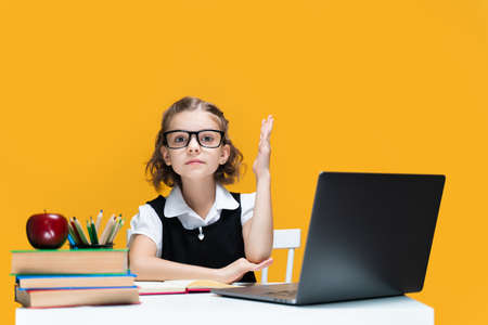 Caucasian schoolgirl raising hand sitting at laptop during online lesson. Distant School Learning.