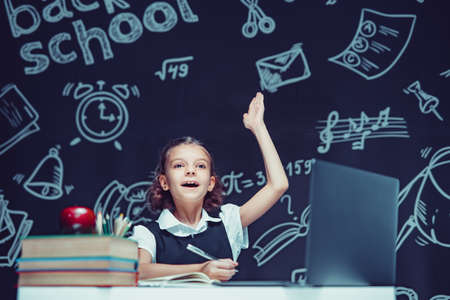 Caucasian schoolgirl raises hand up sits at laptop during online lesson. Distant School Learning.の写真素材