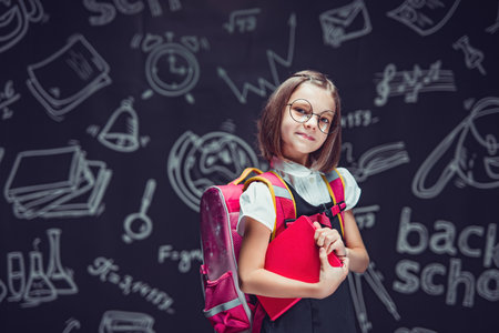 Cute schoolgirl in glasses preparing to go to school with backpack and book in hands Back to schoolの写真素材