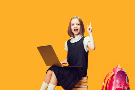 Emotional pupil sits on the stack of books with laptop raises hand with index finger. Kids educationの写真素材