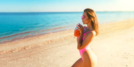 Half lenght young redhead woman in bikini drinking smoothies at the beach. detox concept. Perfect bodyの写真素材