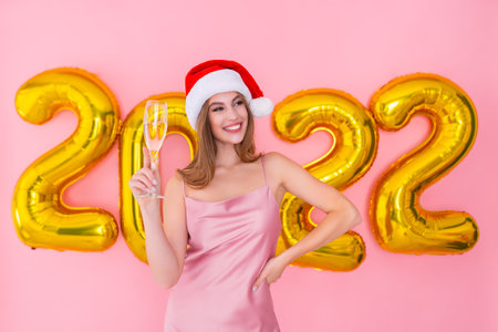 Santa girl holding glass of champagne. Golden numbers air balloons New Year concept