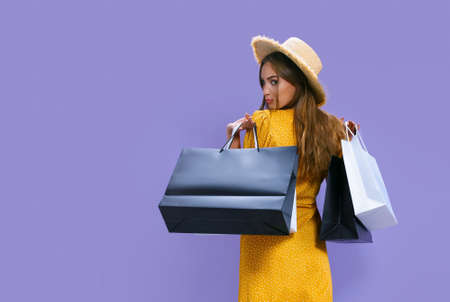 Back view of woman holds packages after shopping on purple background. discount, black Friday, salesの写真素材