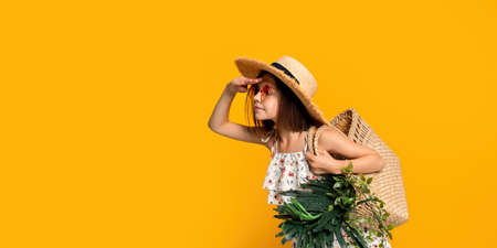 Cute little girl in straw hat in sunglasses holds handbag with tropical plants looking somethingの写真素材